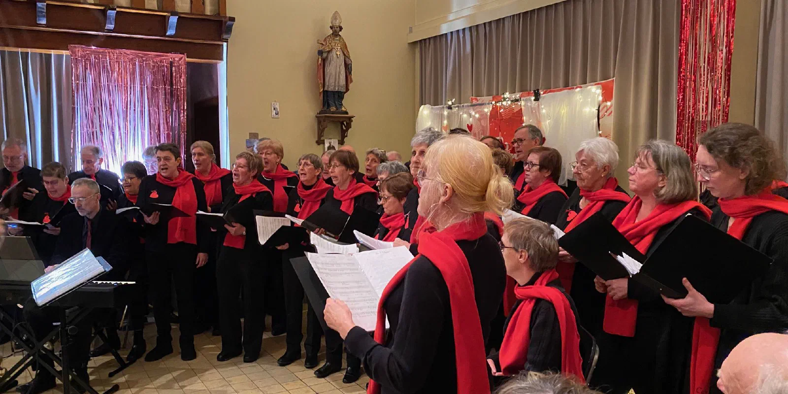 Koor Cantilene, in het zwart met rode sjaals, zingt op het Valentijnsfeest in de Sint-Hendrikskerk; links speelt de pianist