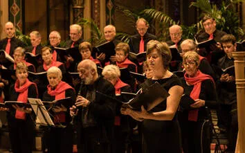 Zangers met rode sjaals zingen uit hun partituren tijdens het winterconcert